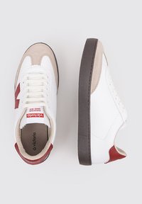 Sneaker bianche con accenti rossi e dettagli in suede beige. Presentano lacci piatti, una suola in gomma marrone scuro e un'etichetta con logo sulla linguetta.