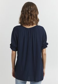 Top leggero blu navy con una vestibilità morbida, caratterizzato da dettagli arricciati sulle spalle e maniche corte a volant.