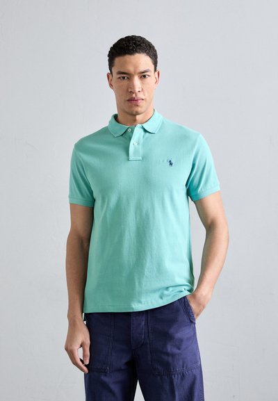 Polo en tissu vert menthe avec un col classique, une patte de boutonnage à deux boutons et un logo brodé sur le côté gauche de la poitrine. Encolure rond, manches courtes.