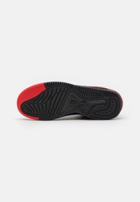 Semelle d'une basket Nike Air noire et rouge montrant des motifs de crampons détaillés et le logo Nike Air centré sur la semelle.