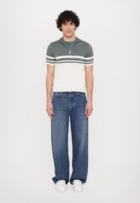 Tight kortärmad polo i mörkgrön och vit med dragkedja; matchad med breda blå jeans och vita sneakers.