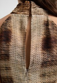 Close-up van een achterrits van een jurk die gedeeltelijk open is, met een bruine en beige dierenprint stof en een keyhole-halslijn.