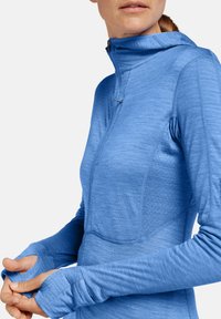 Camiseta atlética de manga larga azul claro con cuello con cremallera, agujeros para los pulgares en las mangas, paneles texturizados y un diseño ajustado.