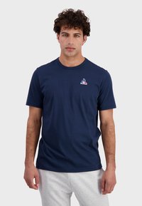 Navy blue cotton t-shirt, short sleeves, crew neckline, featuring a small colorful logo on the chest. Smooth texture, casual fit.