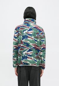 Ζακέτα από φλις με αφηρημένο μοτίβο σε πράσινο, μπλε και μπορντό, ψηλό γιακά και μαλακή υφή, εμφανιζόμενη από πίσω με άνετη εφαρμογή.