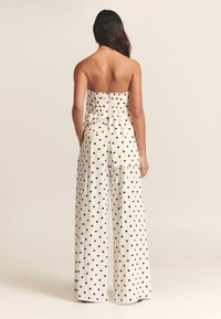 Strapless polka dot jumpsuit with a fitted bodice and wide-leg pants. Made of lightweight fabric, features black dots on a cream background.