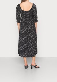 Svart blommig midiklänning med trekvartslång ärm, elastisk midja och djup ryggen. Tyget har små vita blommönster.