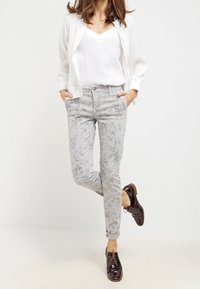 Lättvit jacka över en vit topp, tillsammans med grå byxor med blommönster. Modellen bär mörkbruna snörskor.