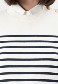 Weißer Pullover mit marineblauen horizontalen Streifen, runder Ausschnitt, gerippte Textur und goldenen Knopfakzenten an der Schulter, kombiniert mit einem weißen Kragen.