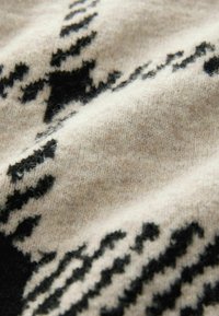 Strikstof med en beige baggrund og sorte geometriske mønstre. Teksturen virker blød og let fuzzy.