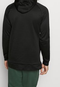 Sudadera con capucha negra de textura suave, mangas largas y corte relajado. Presenta un dobladillo acanalado y un ligero diseño de cola caída.