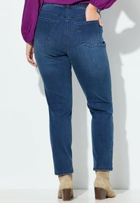 Ciemnoniebieskie dżinsy o dopasowanym kroju, z średnim stanem i dwiema tylnymi kieszeniami. Wykonane z denimu o gładkiej teksturze.