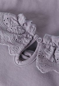 Lila kort shirt met korte mouwen, voorzien van geborduurde kantafwerking met bloemmotieven en een knoopsluiting bij de halslijn. Zachte katoenen textuur.