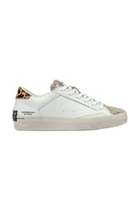 Zapatilla blanca con suela texturizada de color blanco roto; puntera dorada brillante; talón con estampado de leopardo; presenta herrajes negros y texto impreso en el lateral.