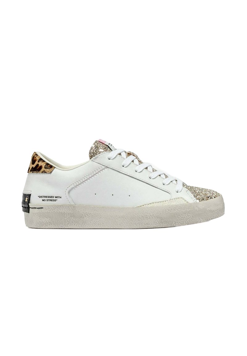 Zapatilla blanca con suela texturizada de color blanco roto; puntera dorada brillante; talón con estampado de leopardo; presenta herrajes negros y texto impreso en el lateral.