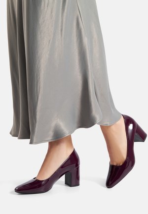 Czerwone bordowe czółenka na słupku z lakierowanej skóry, o kwadratowym nosku, zestawione z miękką, zwiewną srebrną spódnicą z satyny.
