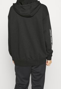 Musta ylipitkä huppari, jossa on nauhakuulokeli, ribbikujat ja helma, mukana valkoista Nike-logoa oikeassa hihassa. Pehmeä materiaali.