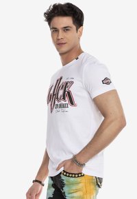 Weißes Baumwoll-T-Shirt mit einem auffälligen schwarzen und roten Grafikdruck. Rundhalsausschnitt und kurze Ärmel mit Logodetail auf dem linken Ärmel.