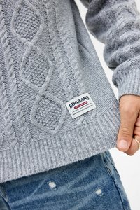 Lys grå strikket sweater med teksturerede kabelmønstre, ribbede cuffs og kant, med en synlig mærketikette, der læser "BDG JEANS."