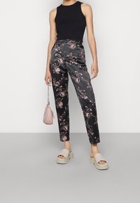 Sorte satinsbukser med pink blomsterprint, tætsiddende pasform og mellemhøj talje, kombineret med en sort ærmeløs top og en lyserød håndtaske.