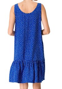 Robe sans manches bleue à pois blancs, avec un ourlet froncé. Le tissu doux tombe librement, atteignant juste au-dessus du genou.