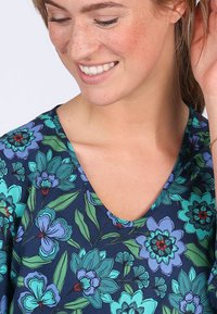 V-neck top in navy fabric with floral print in shades of teal and purple; features green leaves and intricate detailing on flowers.