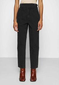 Pantalones de mezclilla negros de talle alto con un diseño de pierna recta, que presentan una costura frontal única y lazos para el cinturón, combinados con botas de tobillo rojas y puntiagudas.