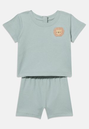 Světlomodrý krátký rukáv a šortky z waffle pleteniny s malou vyšívanou béžovou lví tváří na levé horní části hrudi.