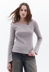 Top grigio chiaro a maniche lunghe con scollatura rotonda, corpo aderente e maniche a campana; realizzato in tessuto morbido con dettagli delle cuciture in vista.