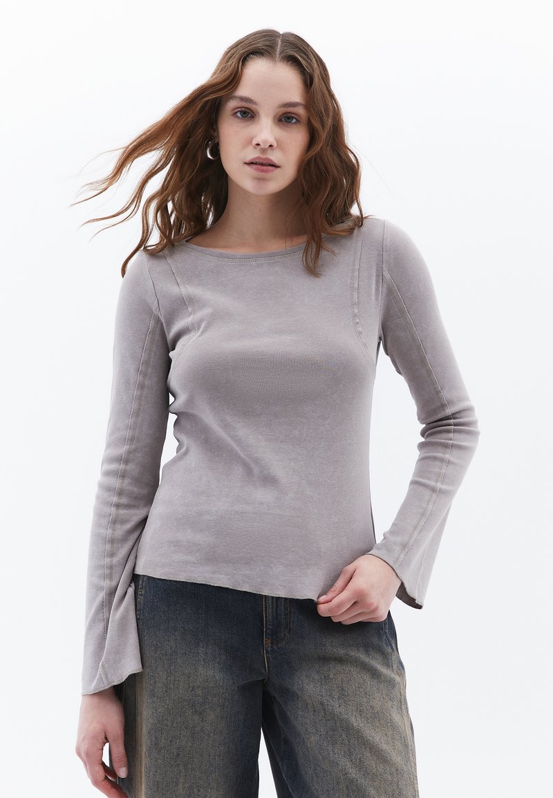 Top grigio chiaro a maniche lunghe con scollatura rotonda, corpo aderente e maniche a campana; realizzato in tessuto morbido con dettagli delle cuciture in vista.