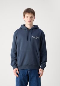 Mørk marineblå hettegenser med lomme foran, har "New York" og "Calvin Klein Jeans" trykt i hvitt. Myk stoffkvalitet og avslappet passform.