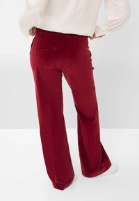 Rode corduroy wijde broek met twee achterzakken. Soepele textuur, hoge taille en een nette zoomafwerking. Draag met witte sneakers.