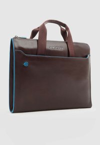 Bolso de cuero marrón con detalles en azul, asas dobles y cierre de cremallera. Cuenta con un bolsillo delantero y un diseño liso y estructurado. Marca Piquadro visible.