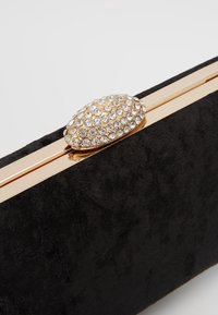 Černé sametové psaníčko se zlatým rámečkem a oválným zapínáním z broušených kamínků. Má hladkou texturu a lesklý povrch kovových částí.