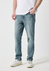 Vaqueros de mezclilla azul claro con un corte recto, que presentan un desvanecimiento sutil y detalles de arrugas. Combinados con zapatillas blancas y una camiseta lisa.