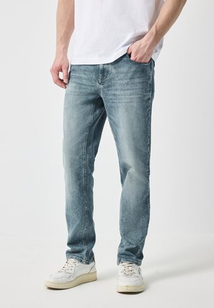Vaqueros de mezclilla azul claro con un corte recto, que presentan un desvanecimiento sutil y detalles de arrugas. Combinados con zapatillas blancas y una camiseta lisa.