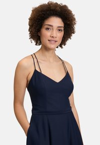 Granatowa sukienka z cienkimi ramiączkami i dekoltem w szpic, posiadająca dopasowaną górę i rozkloszowany dół. Gładka faktura i minimalistyczny design.