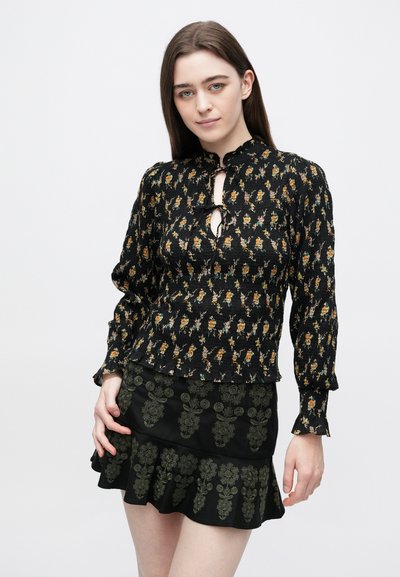 Μαύρο τοπ με μοτίβο λουλουδιών, λαιμόκοψη με άνοιγμα-κλειδί και πτυχωτή υφή, συνδυασμένο με μαύρη φούστα καμπάνα με πράσινη κέντημα.