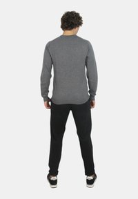 Maglietta grigia a maniche lunghe con scollo rotondo, abbinata a pantaloni neri e sneakers, vista da dietro.