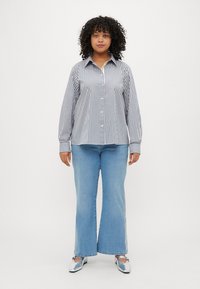 Striped button-up shirt in blue and white, paired with light blue flared jeans. Footwear is silver with a bow detail.
