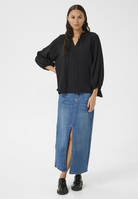 Black textured blouse with a V-neck, button details, and loose sleeves paired with a denim maxi skirt featuring a front slit. Black chunky shoes.