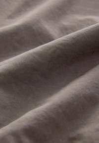 Měkká, texturovaná tkanina v tlumené šedé barvě, zobrazující jemné záhyby a hladký povrch, zdůrazňující její tkané vlastnosti.