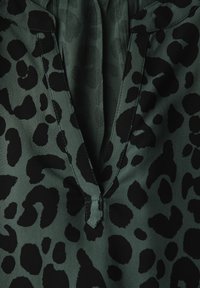 Blusa verde con stampa leopardata nera, caratterizzata da scollatura a V e una sottile texture. I dettagli di cucitura arricchiscono il design.