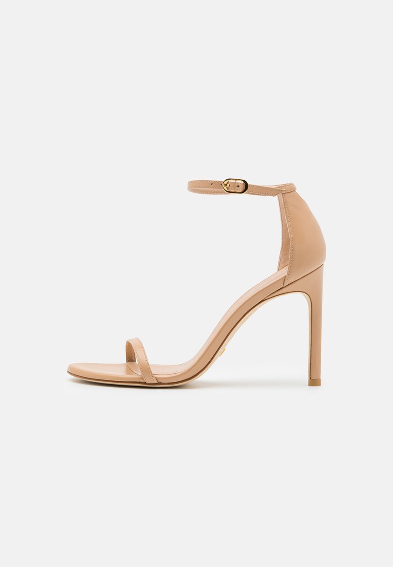 Nude high-heeled sandal with a thin ankle strap, open toe, smooth leather, and a sleek, tapered heel. Minimalist design with gold hardware.