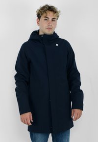 Námornícka modrá nepremokavá bunda s kapucňou, s predným zapínaním na cvočky a logom na hrudi. Hladký materiál a dlhé rukávy.