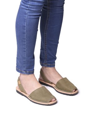 Olive green open-toe shoes with a suede upper, tan leather accents, and a black rubber sole, paired with blue jeans.