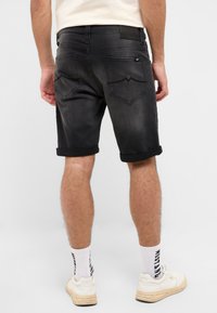 Czarne dżinsowe szorty z podwiniętymi nogawkami, z dwoma tylnymi kieszeniami ozdobionymi przeszyciami. Noszone z białymi skarpetkami i trampkami.