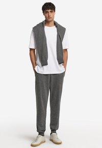 Grå stickad tröja över en vit t-shirt med rund halsringning, kombinerad med grå joggerbyxor och vita sneakers med bruna detaljer.