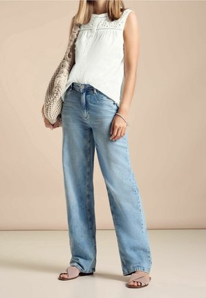 Jeans en jean large bleu clair associés à un haut sans manches blanc avec des détails en œillets, complétés par un sac fourre-tout en osier beige.