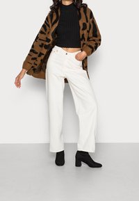 Kardigan med brun och svart djurtryck, svart ribbad crop top, vita vida byxor och svarta klackiga ankelstövlar.